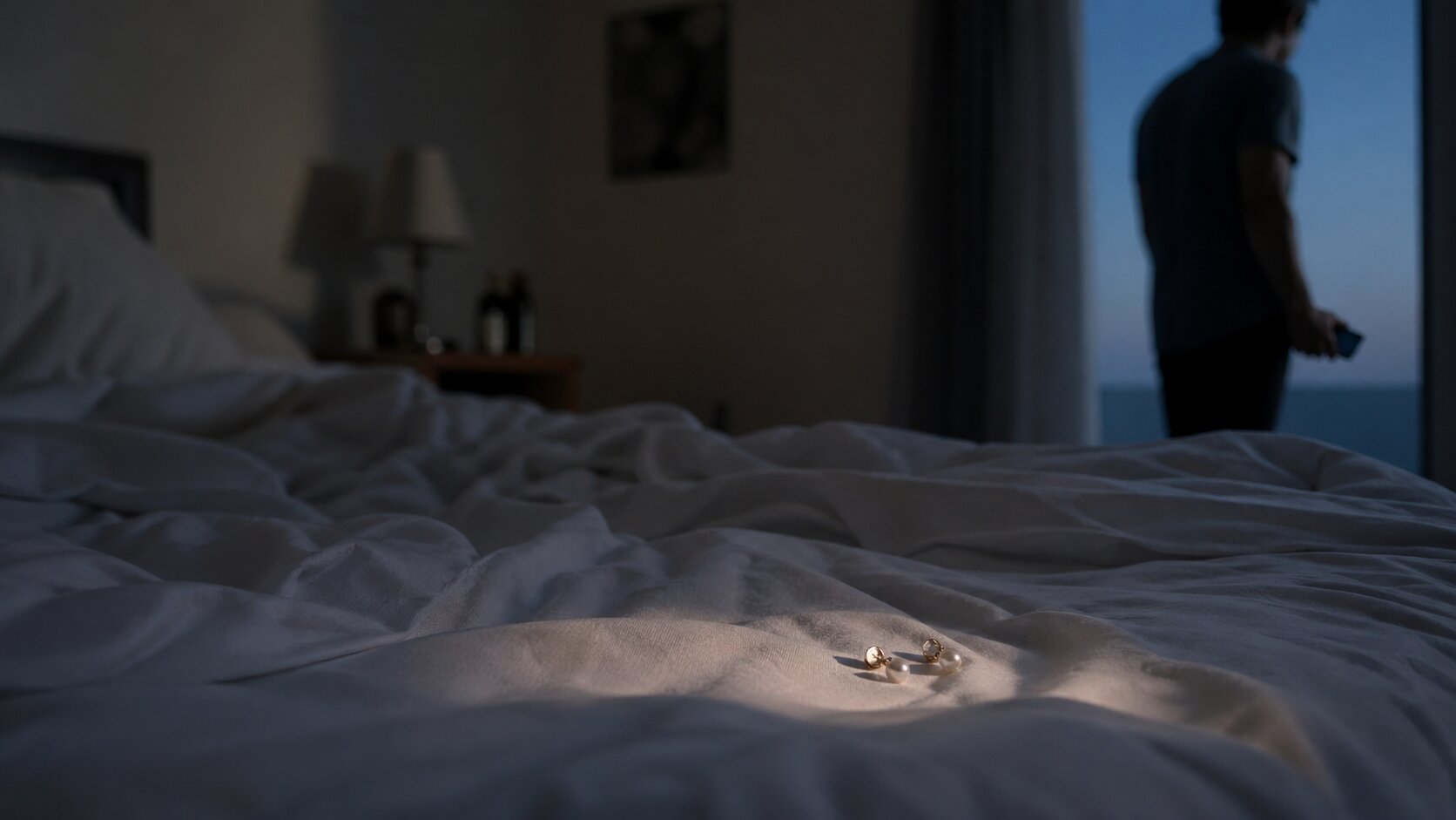 Pair of earrings left in a rumpled bed while a young man hesitates with his phone in a quiet bedroom